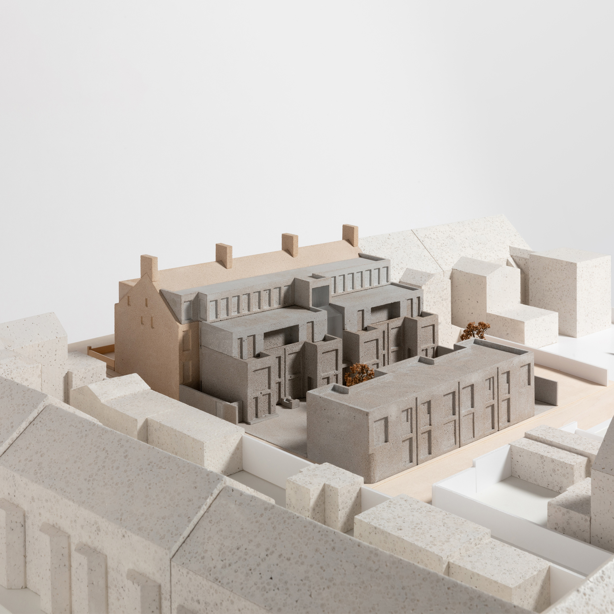 1:100 scale architectural model of the proposed Moseley Passage development, showing the mews courtyard, adjoining retained building, surrounding streetscape, and landscape setting. The proposal is distinguished from the wider context through contrasting materials and finishes, with trees and public realm features represented throughout the model.