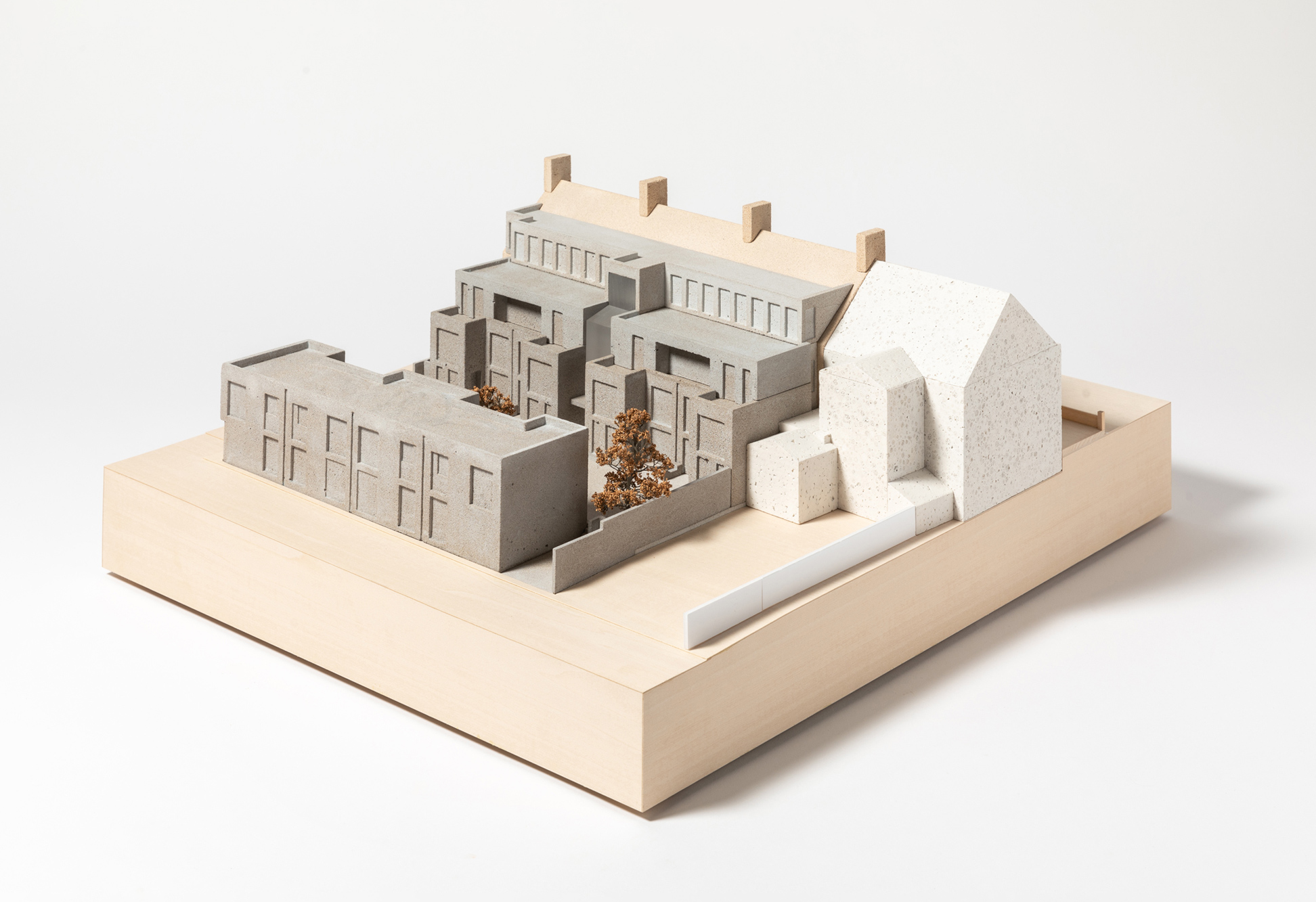 1:100 scale architectural model of the proposed Moseley Passage development, illustrating the mews courtyard, adjoining existing building, and landscape setting. The proposal is represented using contrasting tones and finishes, set on a square base with trees and external spaces shown throughout the model.