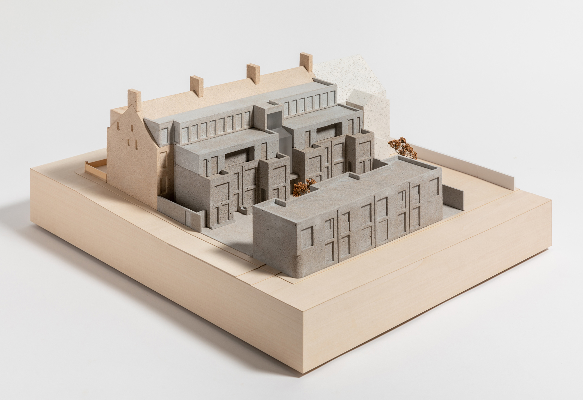 1:100 scale architectural model of the proposed Moseley Passage development, illustrating the mews courtyard, adjoining existing building, and landscape setting. The proposal is represented using contrasting tones and finishes, set on a square base with trees and external spaces shown throughout the model.